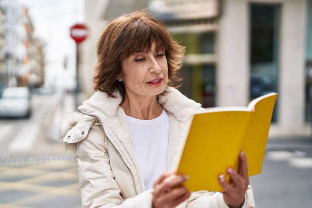 Middelbare leeftijd vrouw lezen boek op straat - Foto, afbeelding