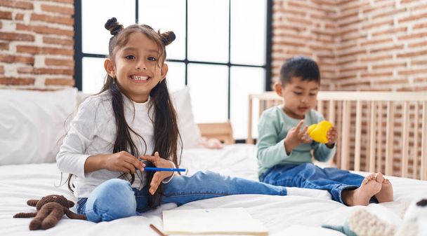 Чарівний хлопчик і дівчина малюють на блокноті, граючи з качиною іграшкою в спальні - Фото, зображення