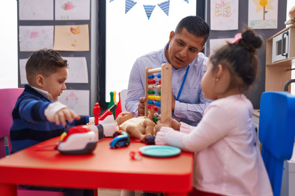 Hispanic man with boy and girl playing with abacus sitting on table at kindergarten - Foto, Imagem