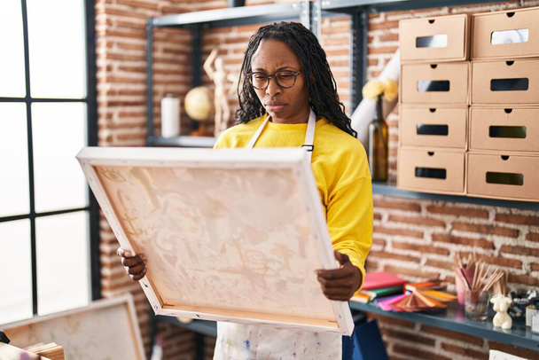 Mujer africana mirando a pintor lienzo escéptico y nervioso, frunciendo el ceño molesto debido a un problema. persona negativa.  - Foto, imagen