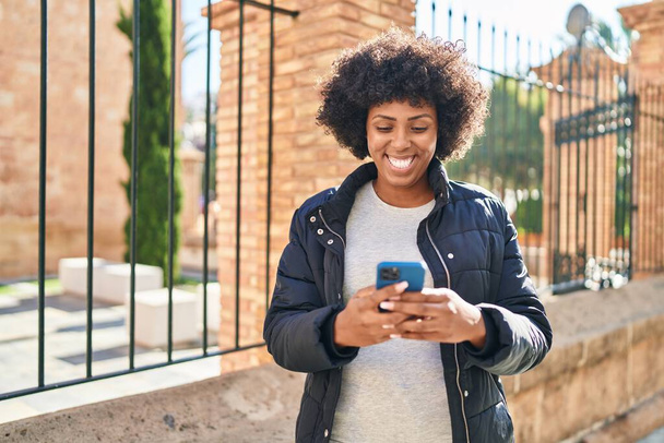 afro-américaine femme souriant confiant en utilisant smartphone à la rue - Photo, image