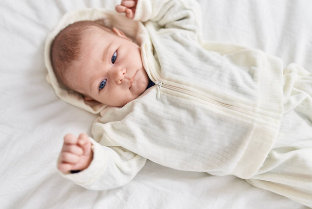 Adorable bebé caucásico acostado en la cama con expresión relajada en el dormitorio - Foto, imagen