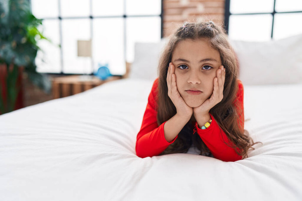 Adorable hispanic girl lying on the bed with sad expression at bedroom - Foto, imagen