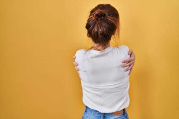 Young beautiful woman wearing casual shirt over yellow background hugging oneself happy and positive from backwards. self love and self care  - Photo, Image