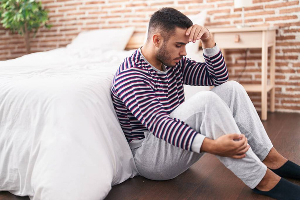 Young hispanic man stressed sitting on floor at bedroom - Foto, immagini