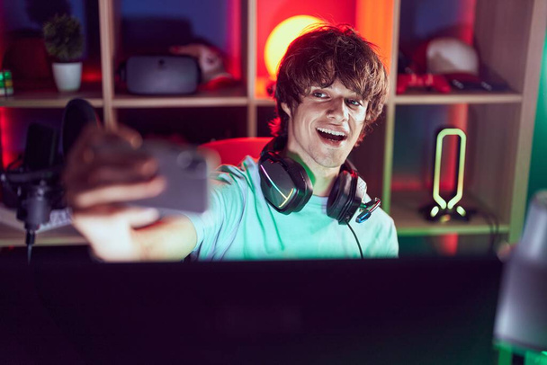 Young blond man streamer smiling confident make selfie by smartphone at gaming room - Fotó, kép