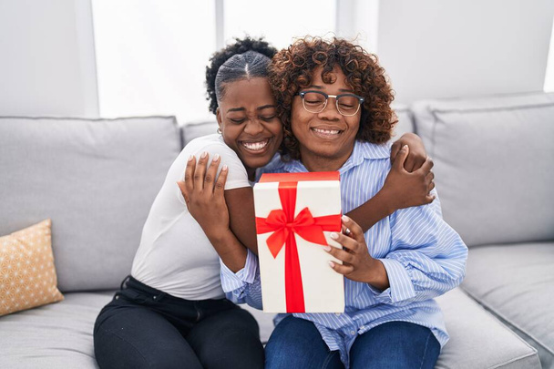 Afro-Amerikan kadın anne ve kızı evde hediyeyle sürpriz yapıyorlar. - Fotoğraf, Görsel