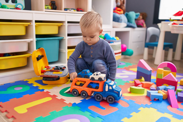 Adorable caucasian boy playing with car toy sitting on floor at kindergarten - Zdjęcie, obraz