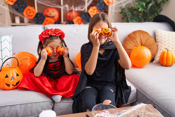 Imádnivaló fiú és lány halloween jelmezt visel, sütőtök kosarakat tart a szeme felett otthon. - Fotó, kép