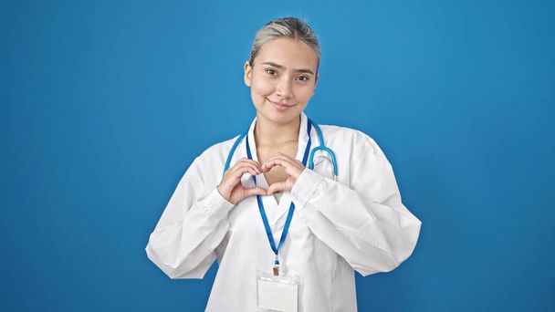 Young beautiful hispanic woman doctor smiling doing heart gesture with hands over isolated blue background - Photo, Image
