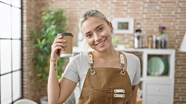 Mladá krásná hispánská žena nosí zástěru drží odnést kávu v jídelně - Fotografie, Obrázek