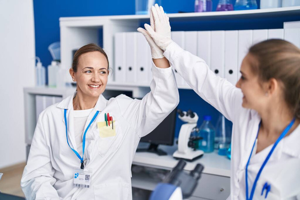 Two women scientists high five with hands raised up at laboratory - Φωτογραφία, εικόνα