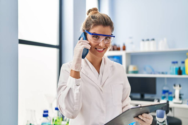 Молода блондинка в уніформі вченого говорить на смартфоні в лабораторії
 - Фото, зображення