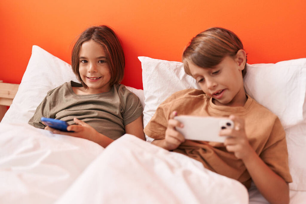 Adorable boys using smartphone sitting on bed at bedroom - Foto, afbeelding
