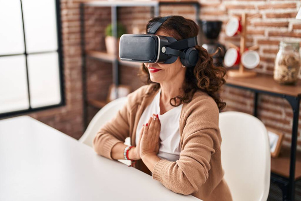 Middle age hispanic woman wearing virtual reality glasses meditating at home - Foto, afbeelding