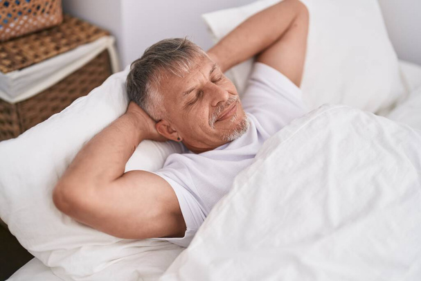 Mężczyzna w średnim wieku siwowłosy leżący na łóżku i śpiący w sypialni - Zdjęcie, obraz