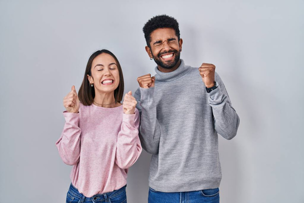 Ein junges hispanisches Paar, das mit erhobenen Armen und geschlossenen Augen aufgeregt vor Erfolg steht und lächelnd den Sieg feiert. Siegerkonzept.  - Foto, Bild