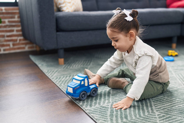 Adorable chica hispana jugando con el juguete del coche sentado en el suelo en casa - Foto, imagen