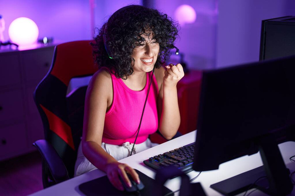 Νεαρή γυναίκα της Μέσης Ανατολής streamer που παίζει βιντεοπαιχνίδι χρησιμοποιώντας υπολογιστή στην αίθουσα τυχερών παιχνιδιών - Φωτογραφία, εικόνα
