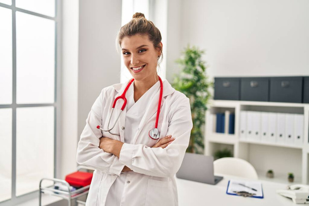 Young blonde woman wearing doctor uniform standing with arms crossed gesture at clinic - Foto, afbeelding