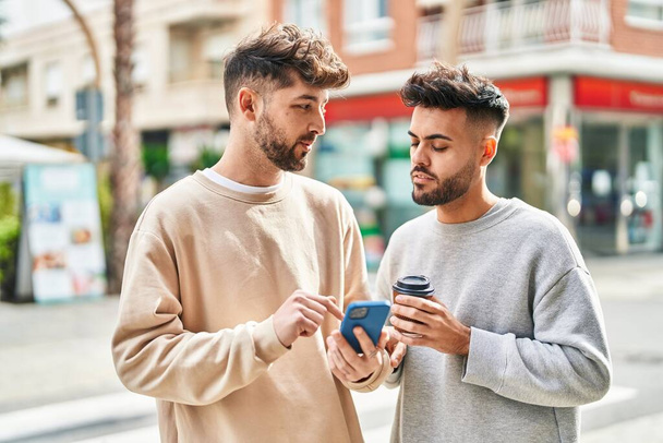 Young couple using smartphone and drinking coffee standing together at street - Photo, image