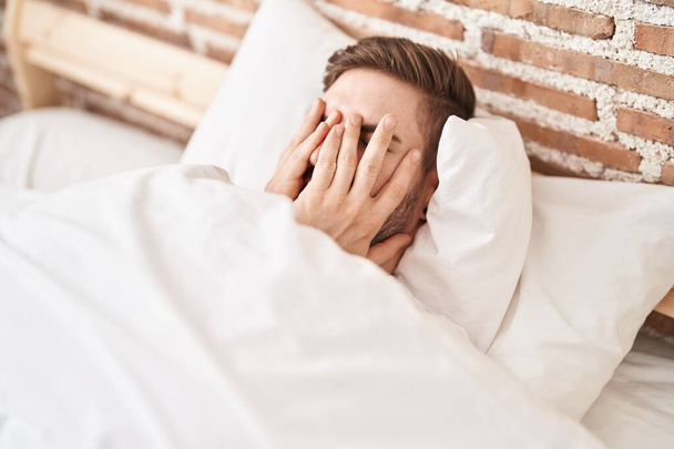 Young caucasian man stressed lying on bed at bedroom - Photo, image