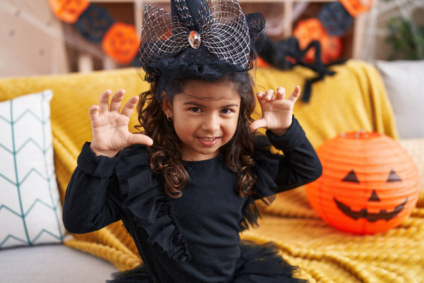 Adorable hispanic girl having halloween party doing scare gesture at home - Фото, изображение