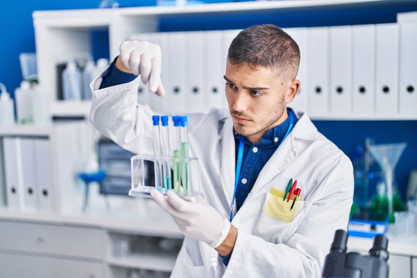 Young hispanic man scientist holding test tubes at laboratory - Foto, Imagen