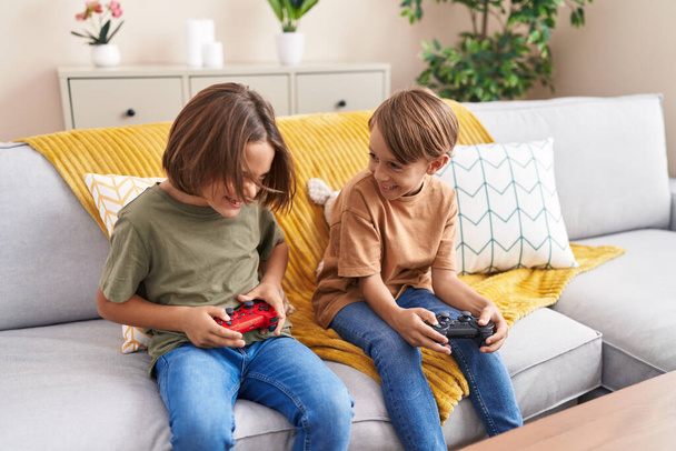 Adorables garçons jouant à un jeu vidéo assis sur le canapé à la maison - Photo, image