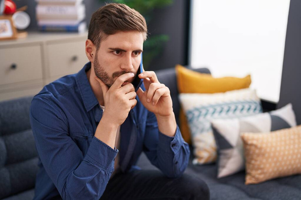 Young caucasian man talking on smartphone with worried expression at home - Photo, Image