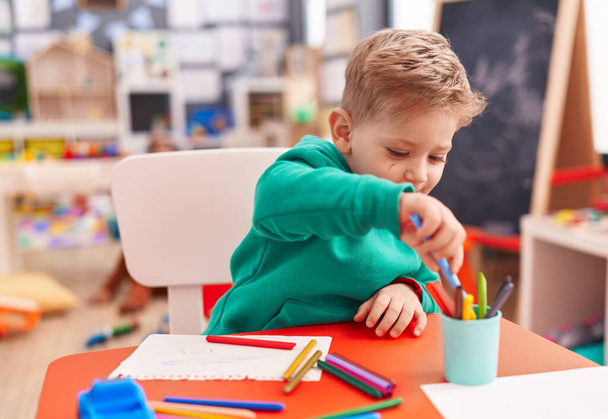 Adorable niño caucásico estudiante de preescolar sentado en el dibujo de la mesa en el cuaderno en el jardín de infantes - Foto, Imagen