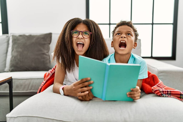 Zwei Geschwister, die wütend auf dem Sofa liegen und ein Buch lesen, schreien frustriert und wütend, schreien vor Wut. Wut und aggressives Konzept.  - Foto, Bild