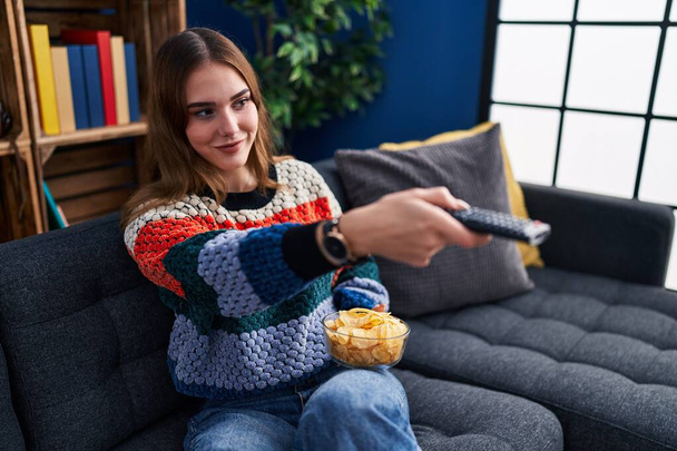 Молода жінка дивиться фільм, сидячи на дивані вдома
 - Фото, зображення