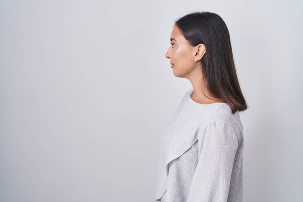 Junge hispanische Frau, die über weißem Hintergrund steht und zur Seite schaut, entspannte Profilpose mit natürlichem Gesicht und selbstbewusstem Lächeln.  - Foto, Bild