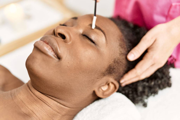 Африканська американка лежить на масажному столі, а брови лікують у салоні краси. - Фото, зображення