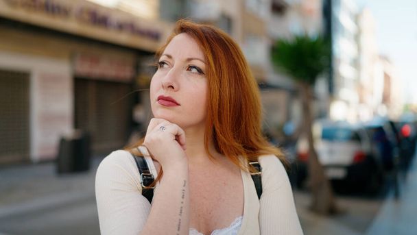 Young redhead woman standing with doubt expression at street - Fotografie, Obrázek