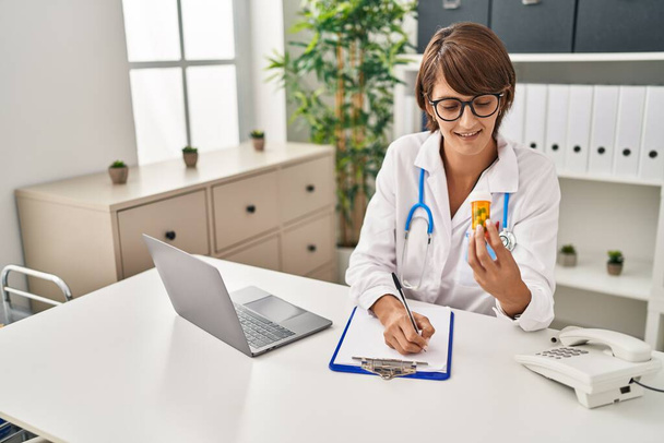 Nuori kaunis latino nainen lääkäri tilalla pillereitä pullon kirjallisesti asiakirjan klinikalla - Valokuva, kuva