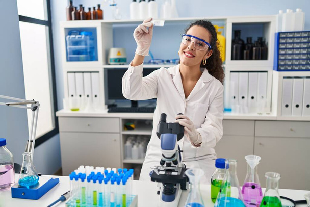 Young beautiful hispanic woman scientist smiling confident looking sample at laboratory - Foto, Imagen