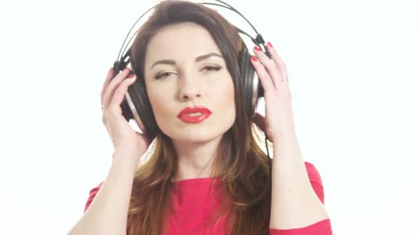 Pretty woman wearing red lipstick listening to the music touching big headphones takes off ear cup saying what isolated on white background medium shot - Footage, Video