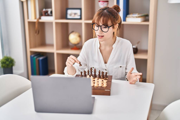 Νεαρή γυναίκα παίζει online παιχνίδι σκάκι στο σπίτι - Φωτογραφία, εικόνα