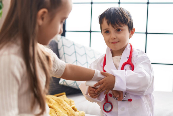 Suloinen poika ja tyttö yllään lääkäri yhtenäinen bandaging käsivarsi kotona - Valokuva, kuva