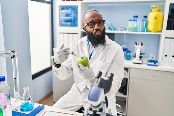 African american man working at scientist laboratory with apple looking at the camera blowing a kiss being lovely and sexy. love expression.  - Foto, Imagen