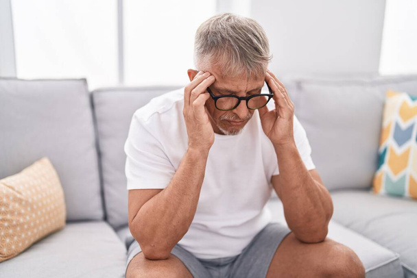 Homem de cabelos grisalhos de meia idade estressado sentado no sofá em casa - Foto, Imagem
