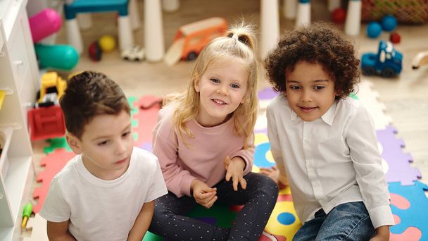 Grupa dzieci siedzi na podłodze uśmiechnięta pewnie w przedszkolu - Zdjęcie, obraz
