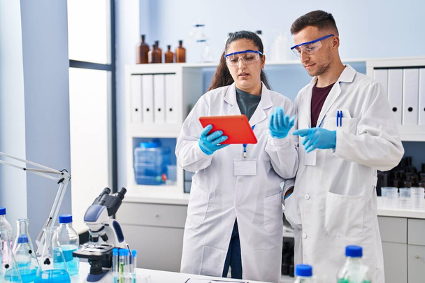 Man and woman wearing scientist uniform using touchpad at laboratory - Foto, imagen