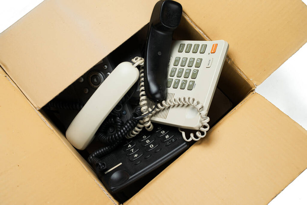 Vieux téléphones de bureau dans une boîte en carton. Sur fond blanc
.  - Photo, image