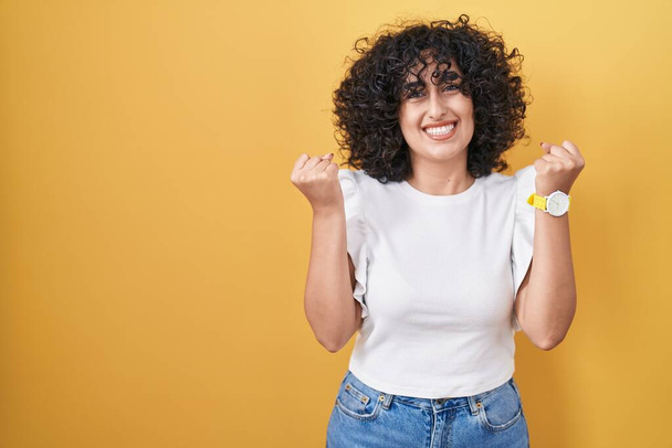 Young middle east woman standing over yellow background celebrating surprised and amazed for success with arms raised and open eyes. winner concept.  - Фото, изображение