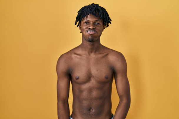 Jonge Afrikaan met dreadlocks, staande blaaskaken zonder shirt met grappig gezicht. mond opgeblazen met lucht, gekke uitdrukking.  - Foto, afbeelding