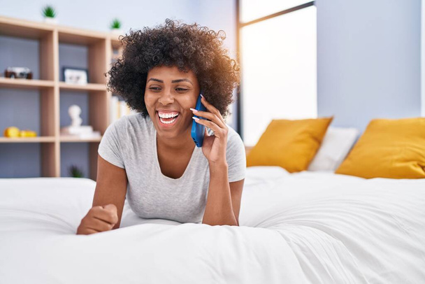 African american woman talking on smartphone lying on bed at bedroom - Фото, зображення