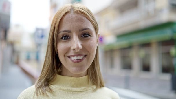 jonge blonde vrouw glimlachen zelfverzekerd staan op straat - Foto, afbeelding